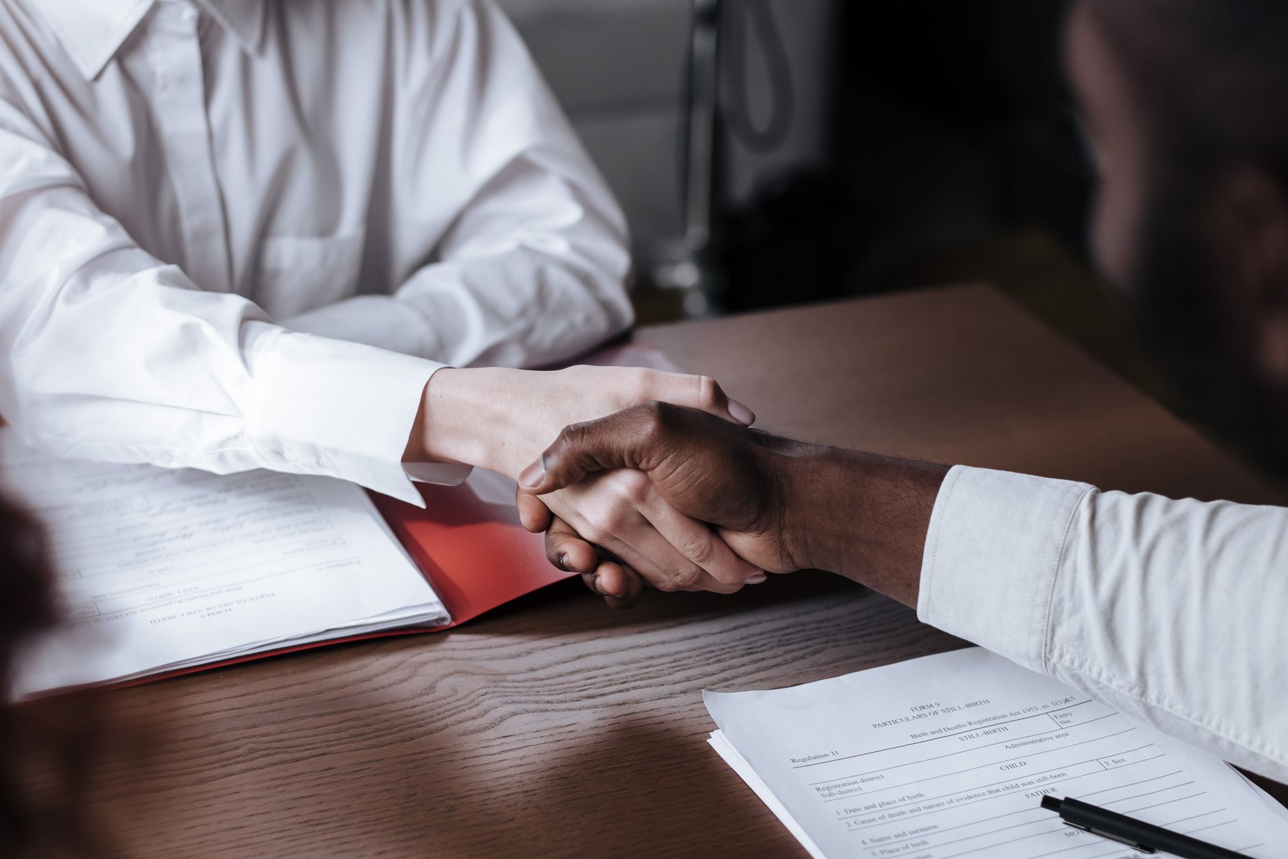 Two people shaking hands across a table after an interview
