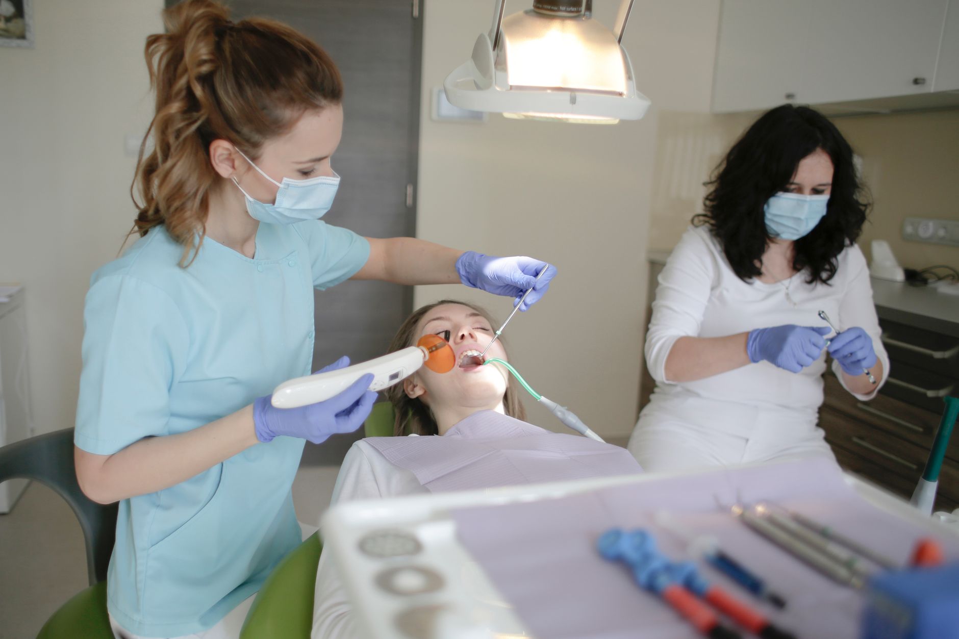 Dental assistant using a curing light while a colleague prepares instruments